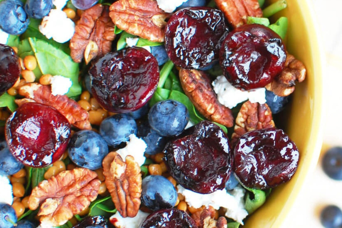 image taken from above of a BBQ Balsamic cherry, goats cheese and green lentil spinach salad in a bowl on a white surface with some cherries loose to the side